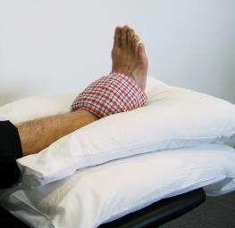 Leg up on pillow with cold pack over ankle